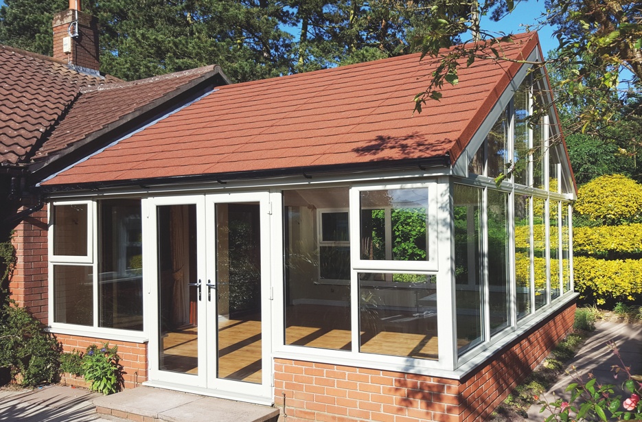 A spacious and elegant tiled conservatory with a refined interior design, featuring plush seating, a coffee table, and a contemporary decor, seamlessly blending the comfort of indoor living with the natural beauty visible through the large glass windows.